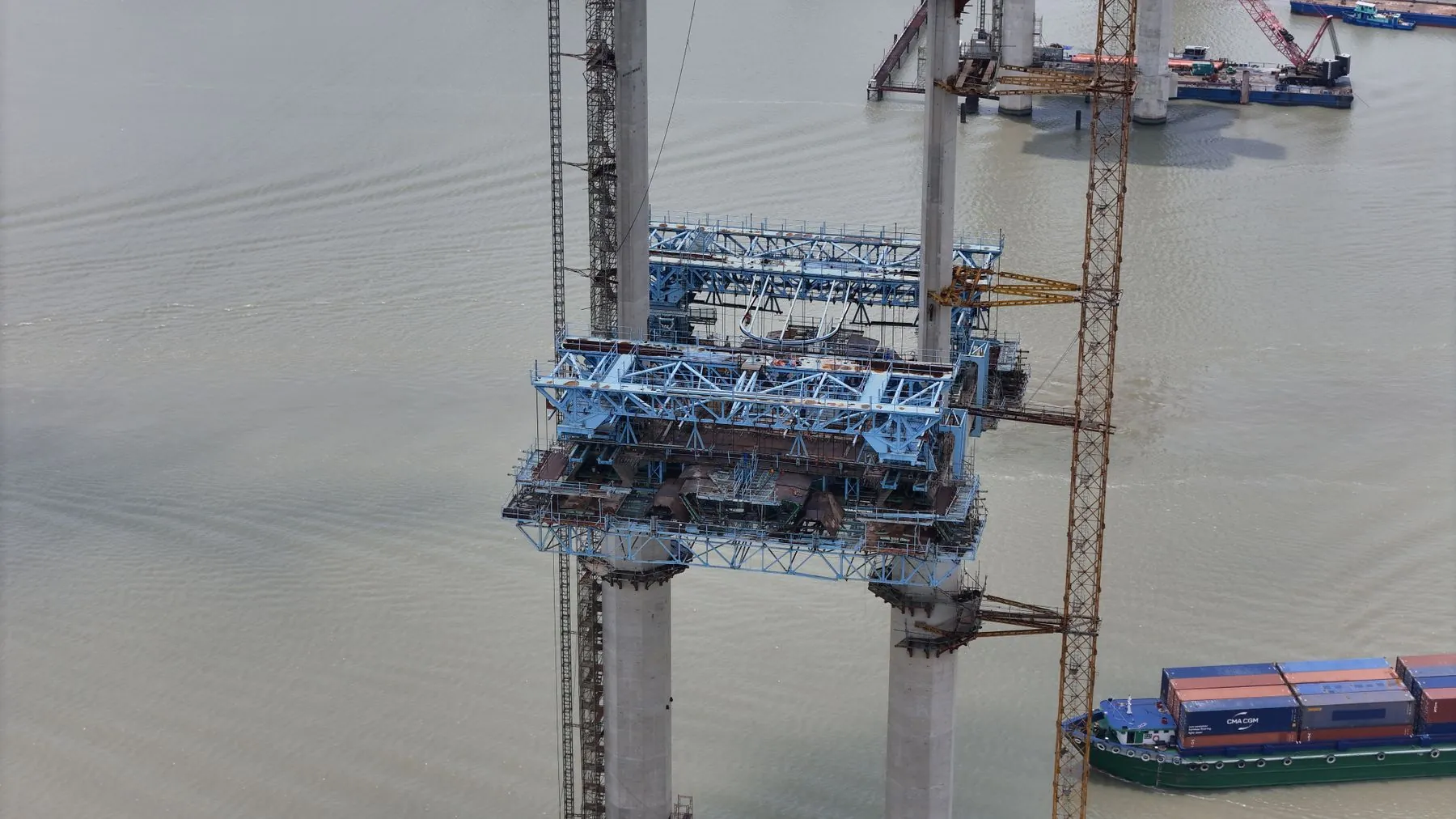 An aerial view of bridge construction over a river with a barge below