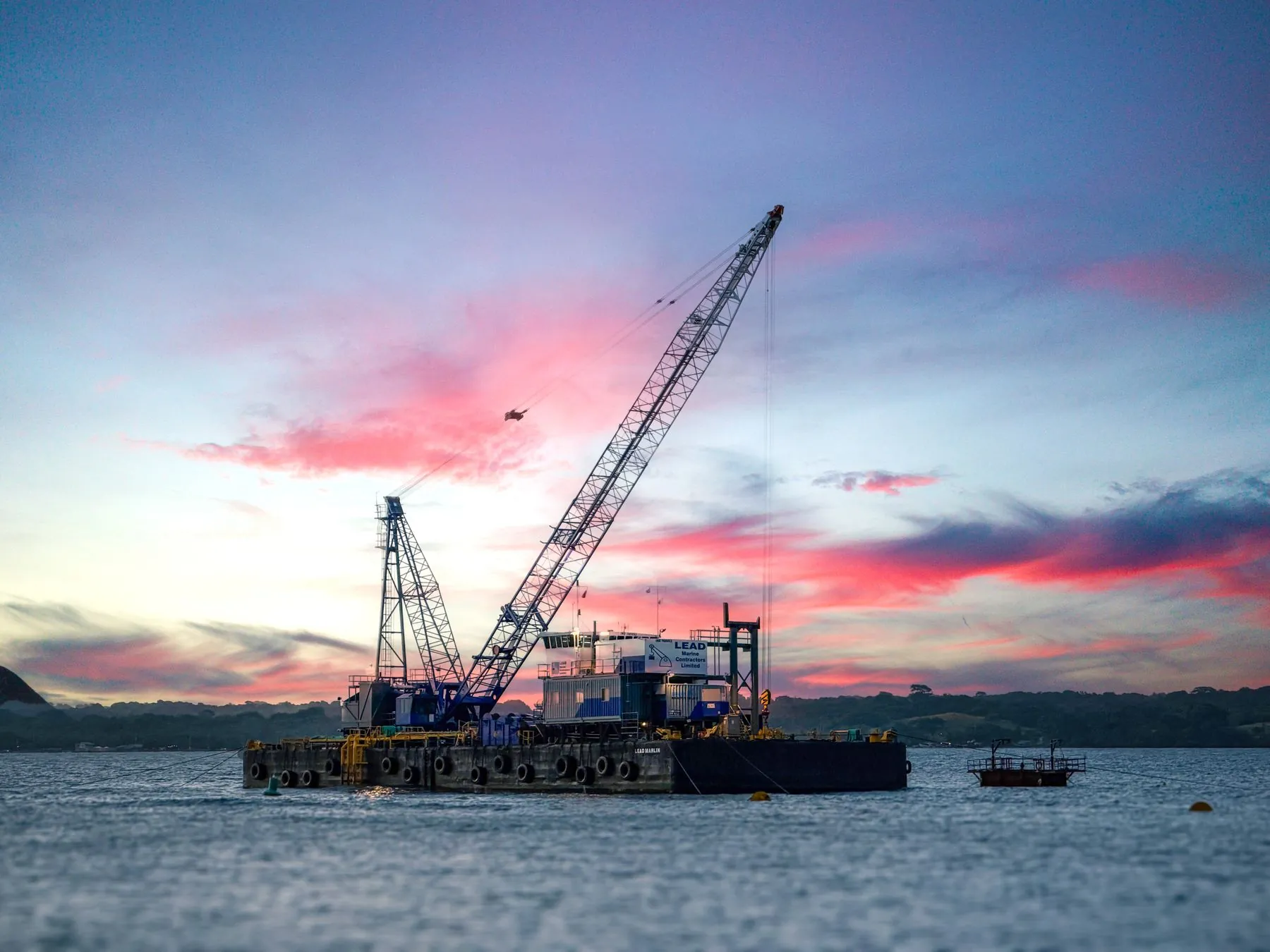 A crane barge on the water at sunset
