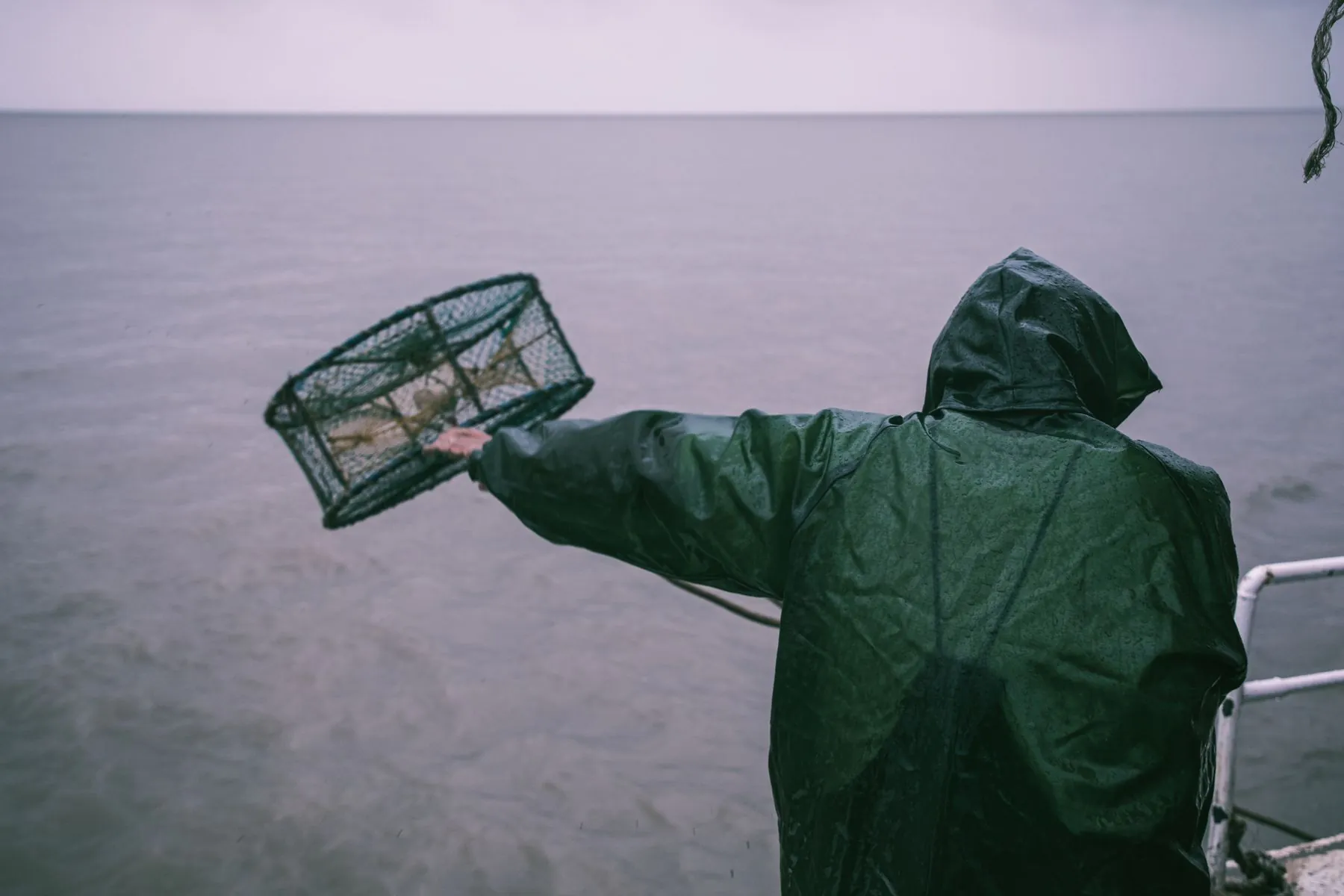 A fisherman in rain gear throwing a crab pot over the side