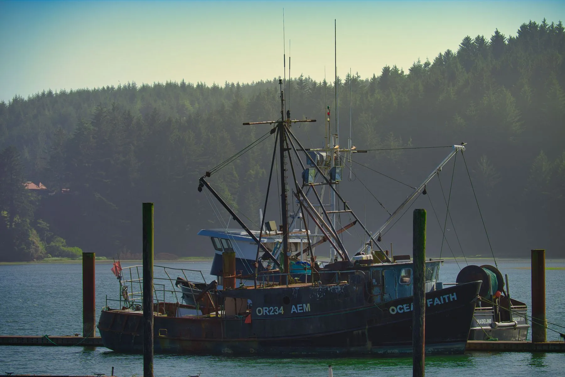 A commercial fishing boat tied up at a dock in Oregon with forested hills behind