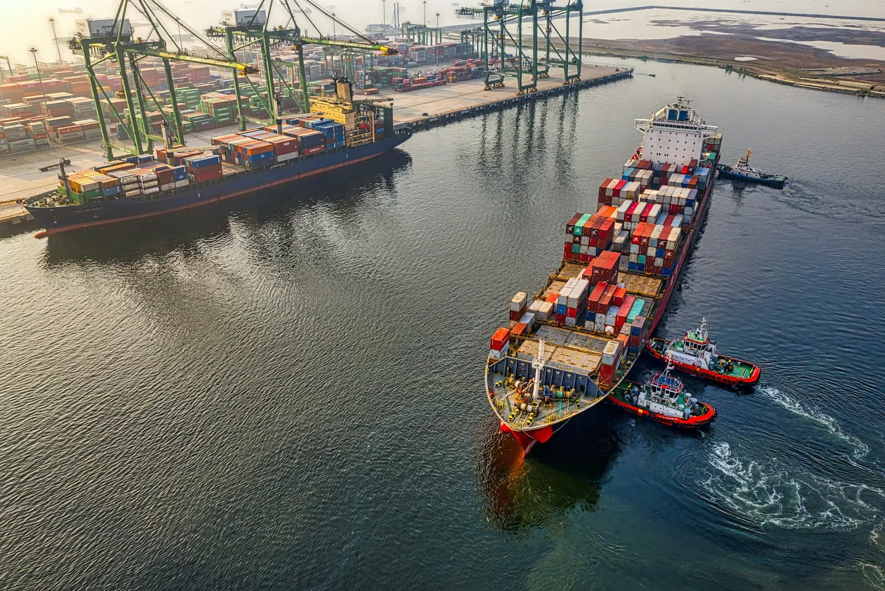 An aerial view of tugboats guiding a container ship into a port terminal