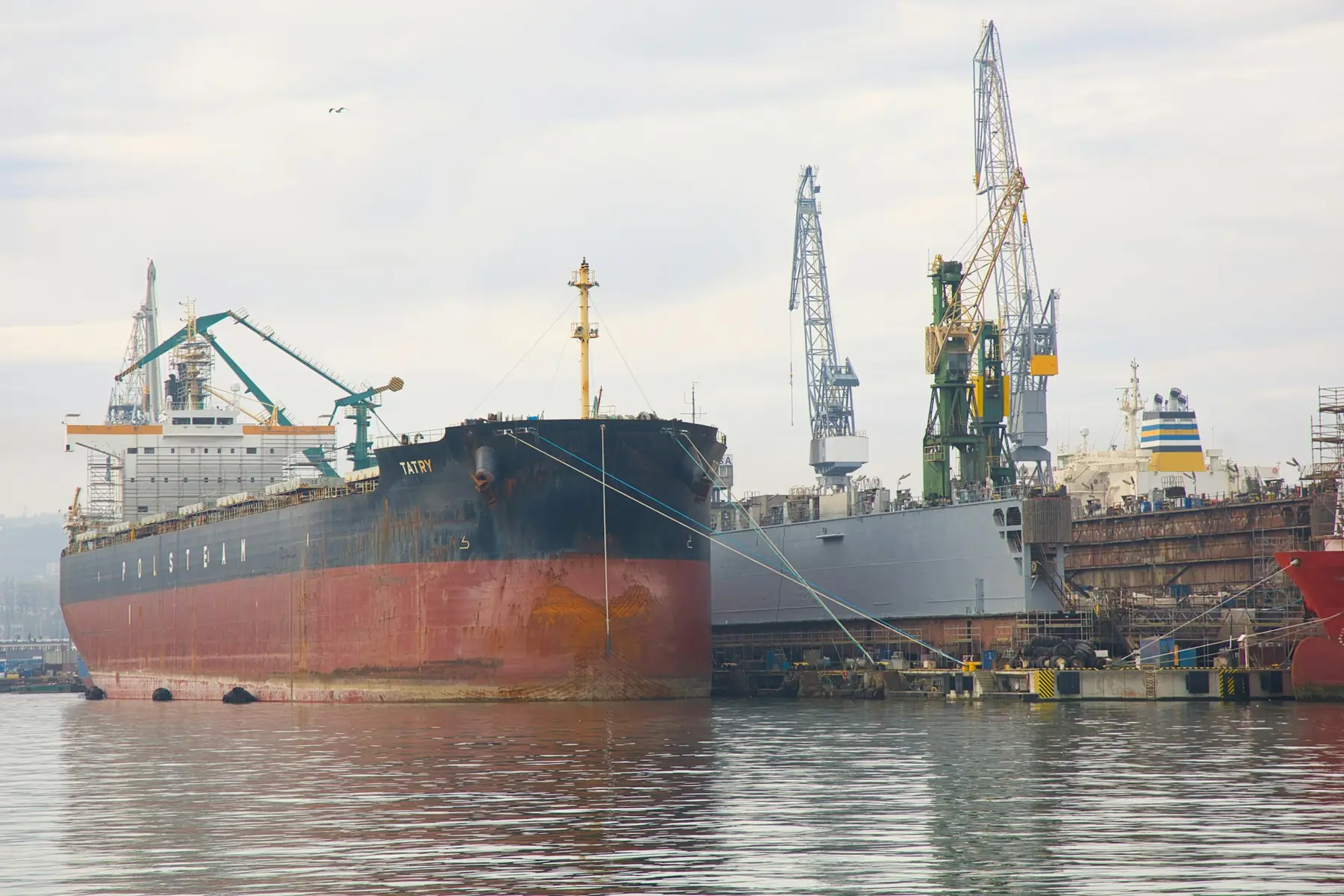A cargo ship moored at a shipyard quay beside cranes