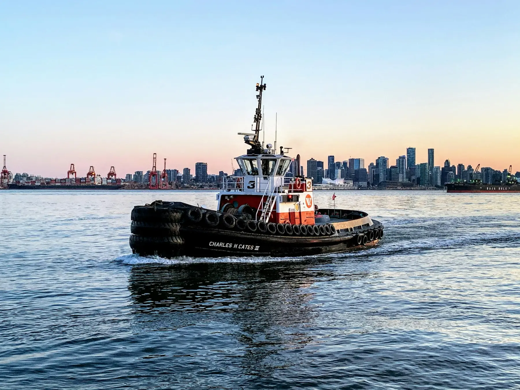 A tugboat crossing a harbor in front of a city skyline